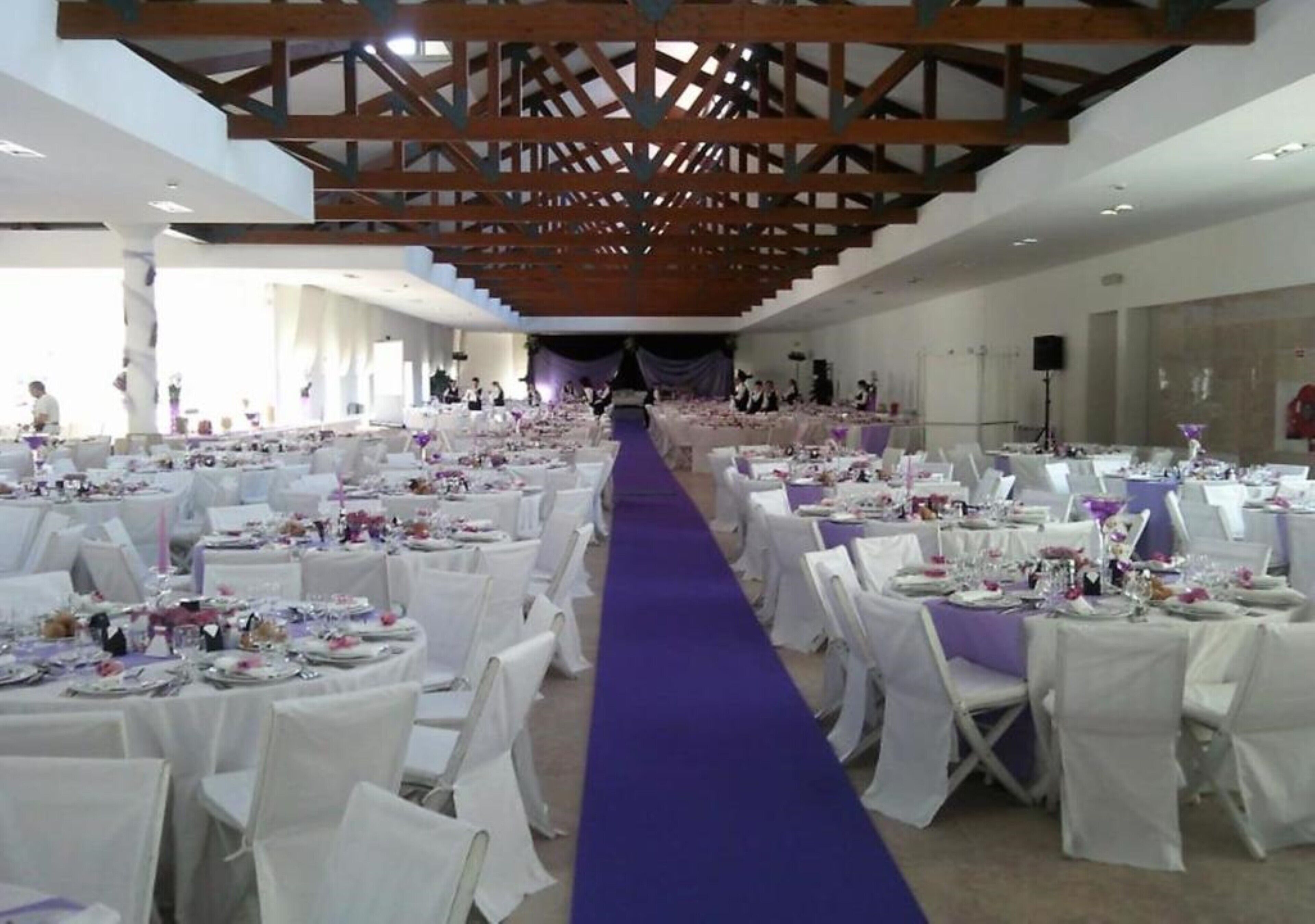 A banquet hall with round tables covered in white tablecloths and purple runners, arranged in rows.