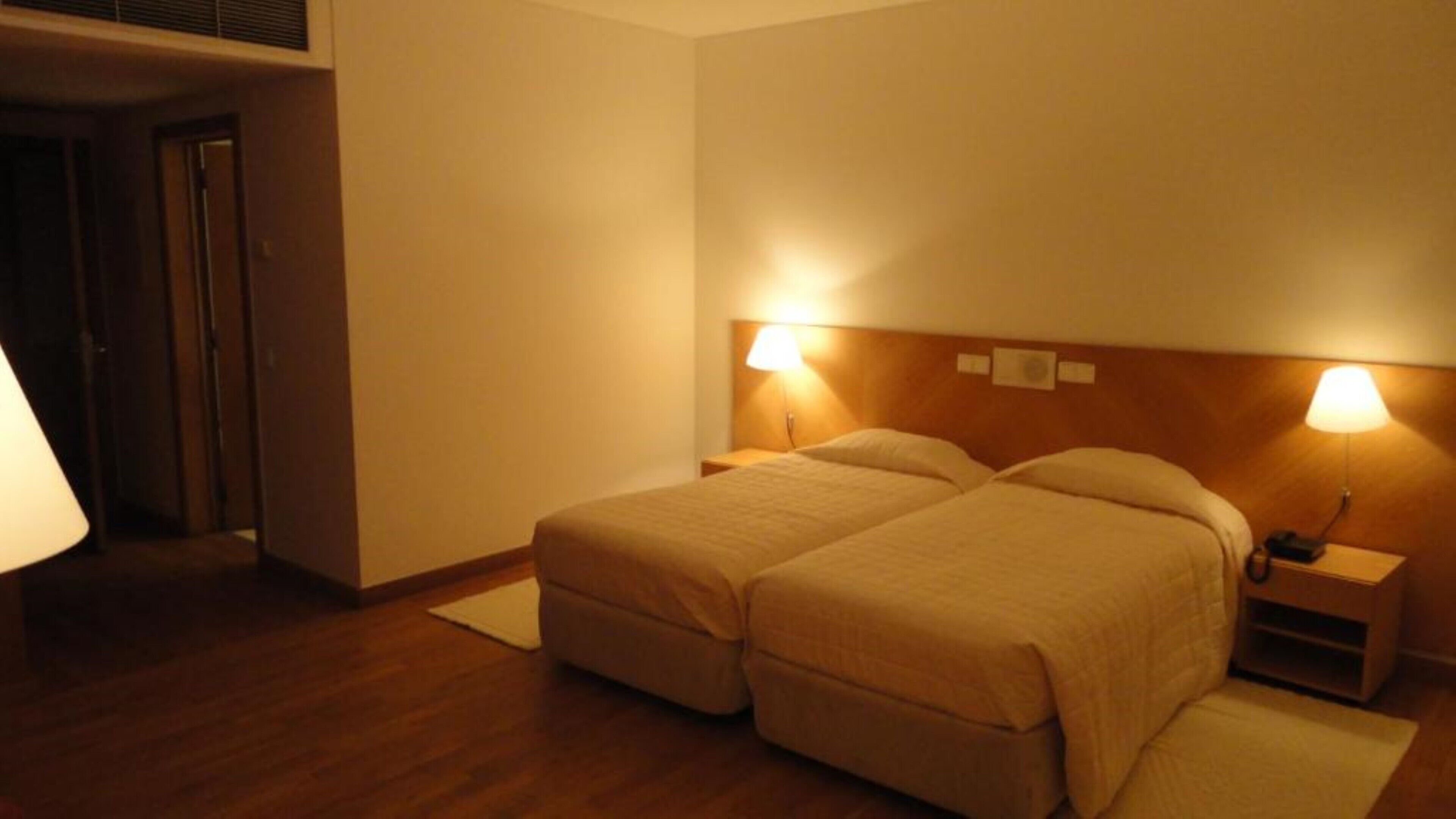 A hotel room with two beds, a nightstand, and a lamp.