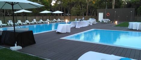 A poolside area with lounge chairs, umbrellas, and tables set up for an event.