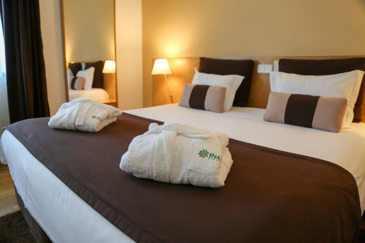 A hotel room with two beds, brown bedding, white towels, and a mirror on the wall.