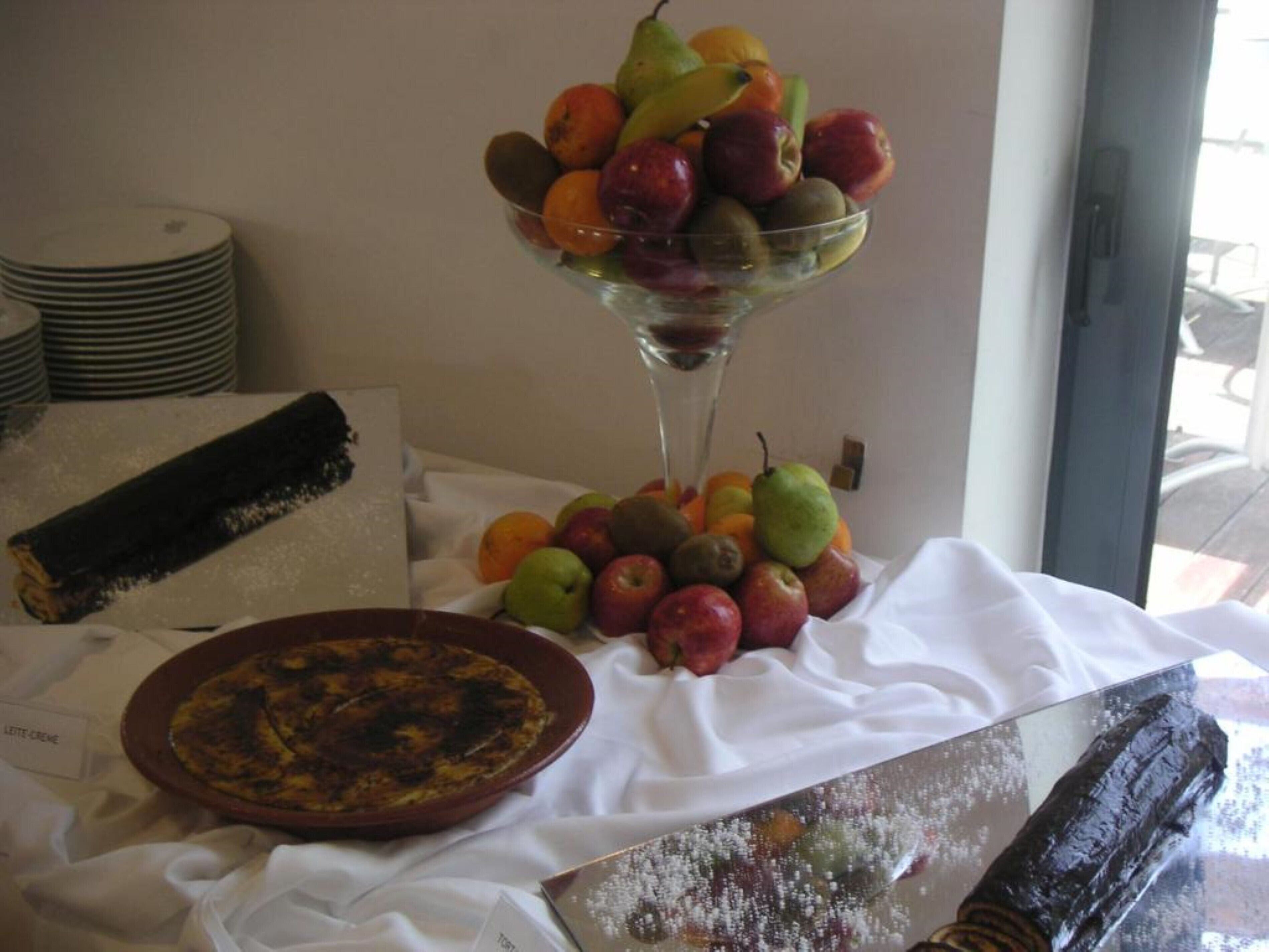 A table with a fruit bowl, a plate of food, and a rolled-up menu.