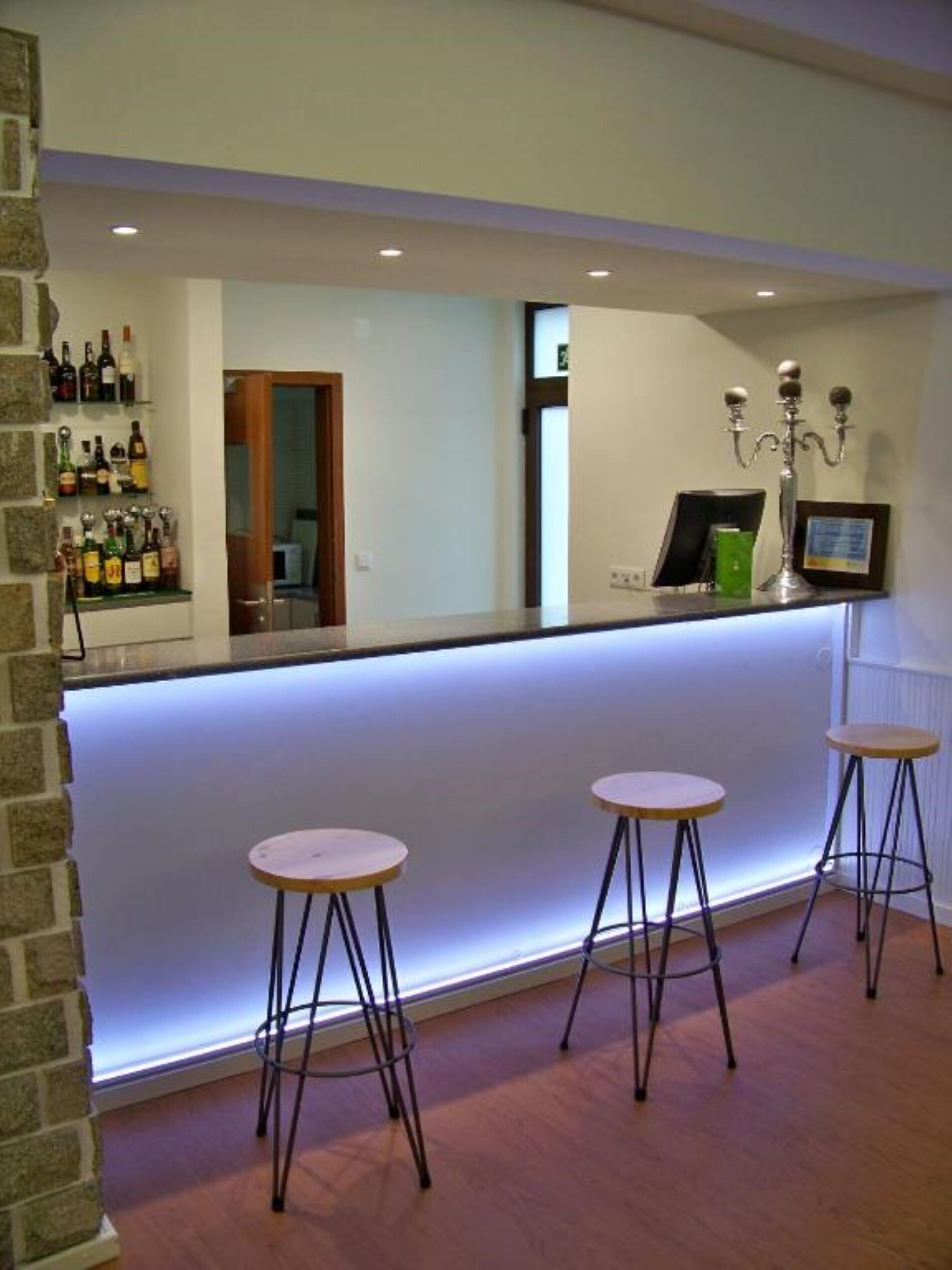 A bar area with a counter, three stools, and a wall-mounted shelf with bottles.