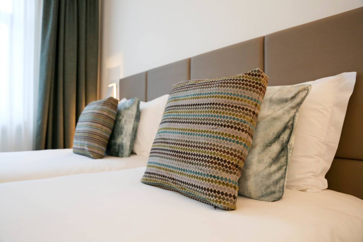 A neatly made bed with white sheets and multiple pillows, including a patterned one.