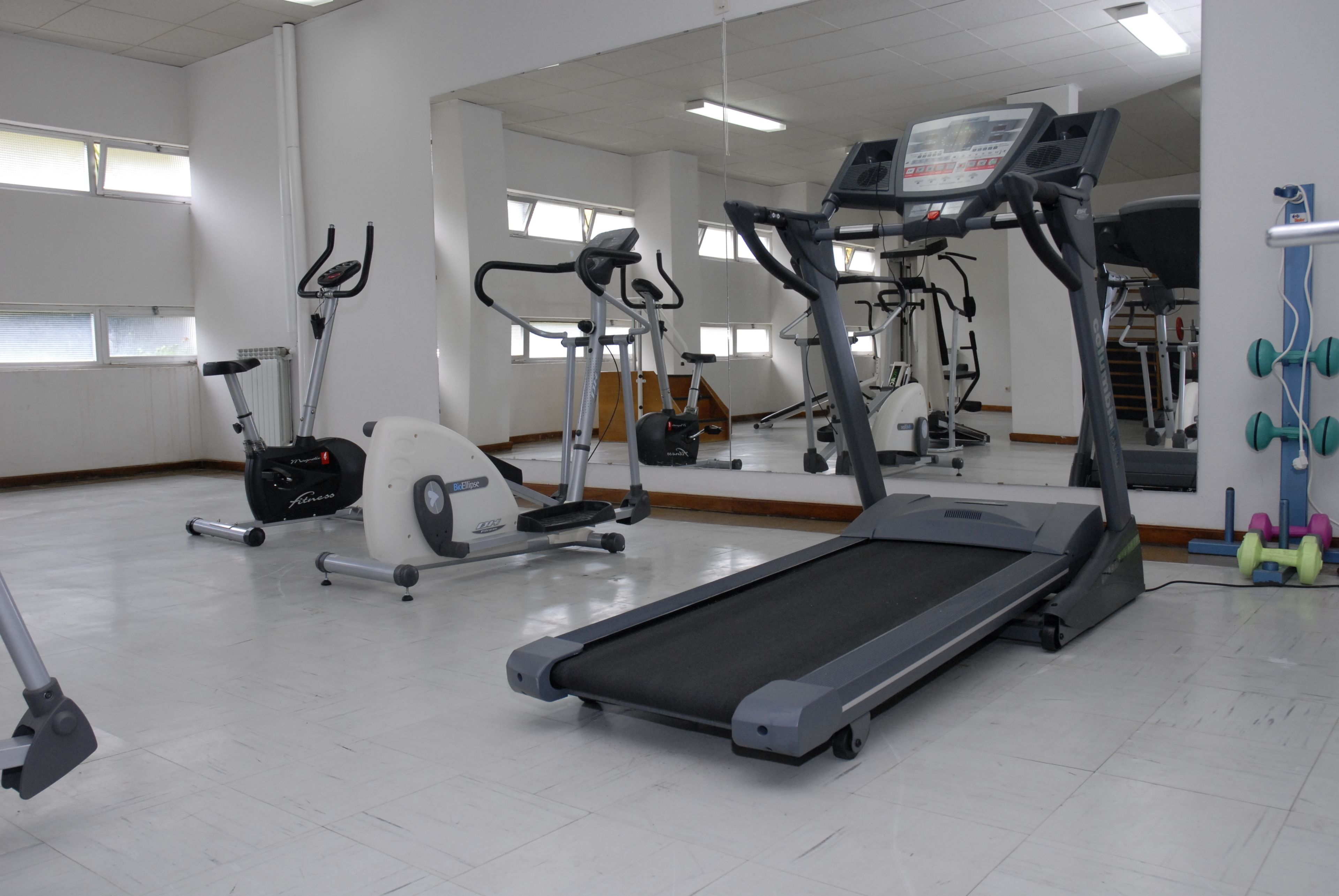 Een sportschool met diverse fitnessapparaten, waaronder loopbanden en hometrainers.
