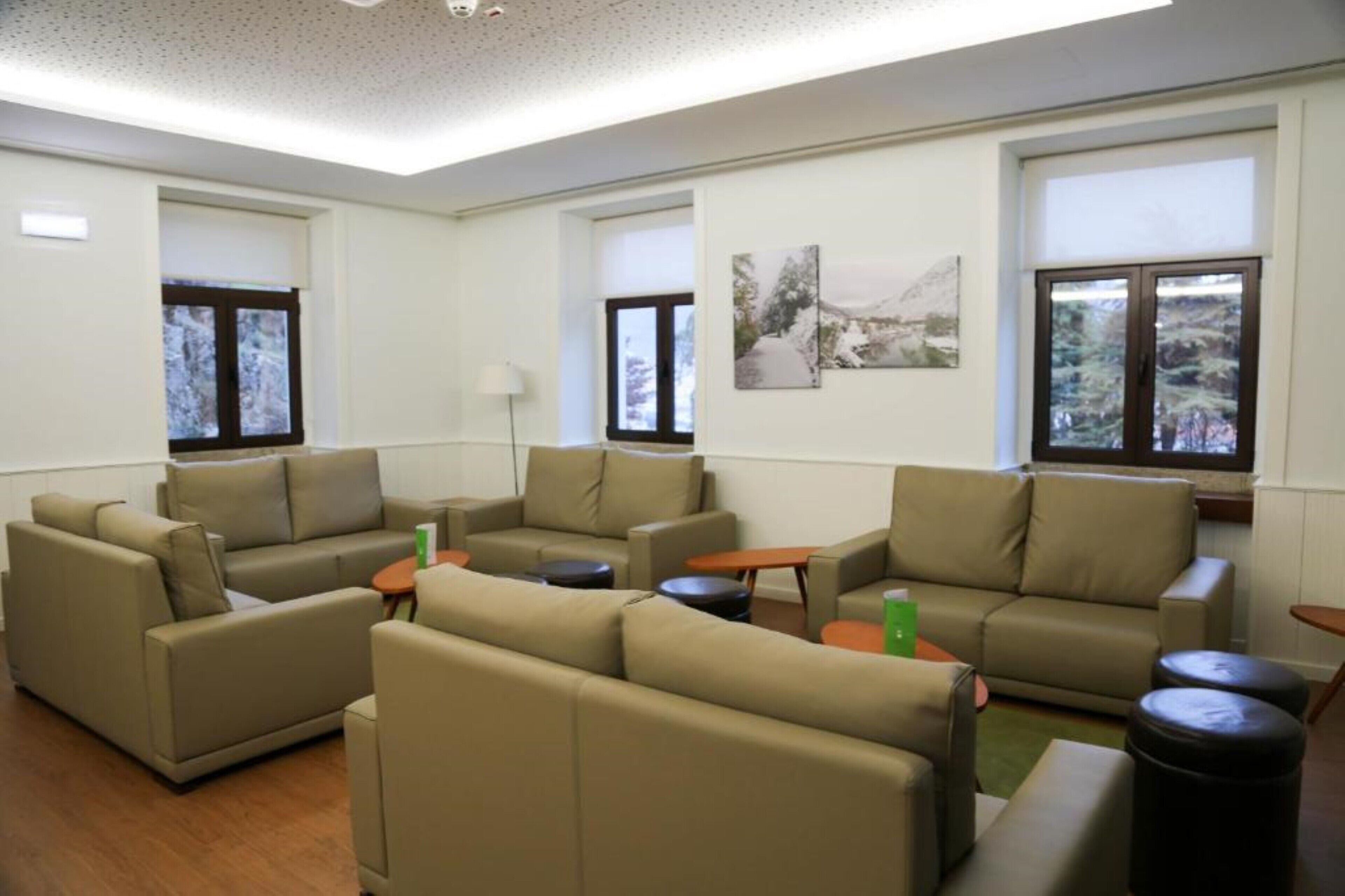 A spacious living room with multiple sofas and a coffee table, large windows with views of trees, and a painting on the wall.