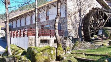 A rustic building with a large water wheel, surrounded by trees and rocks.