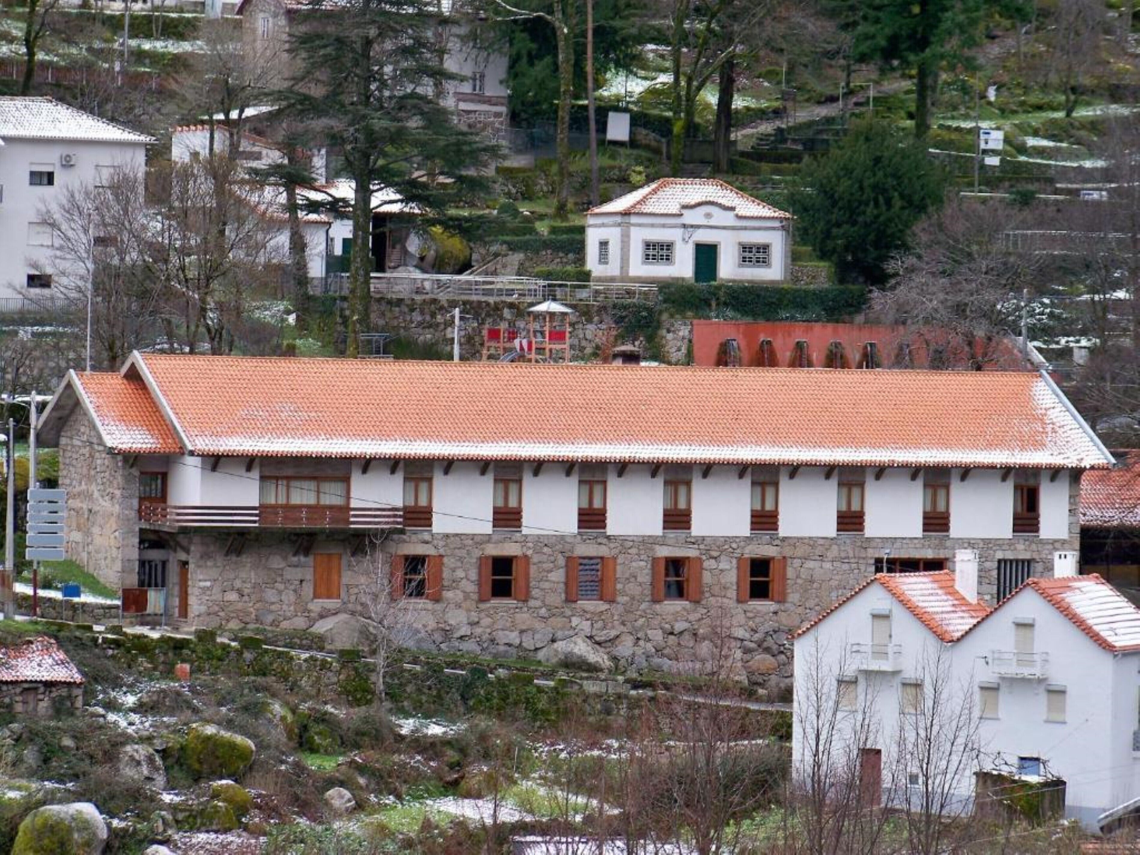 A stone building with a red-tiled roof, multiple windows, and a small balcony.