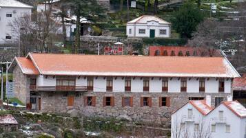 A stone building with a red-tiled roof, multiple windows, and a small balcony.