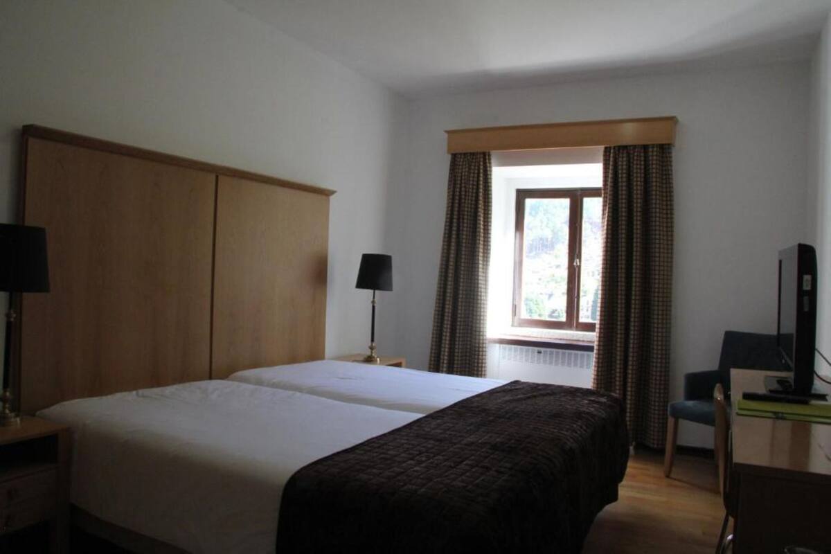 A hotel room with two beds, a desk with a chair, a TV, and a window with curtains.