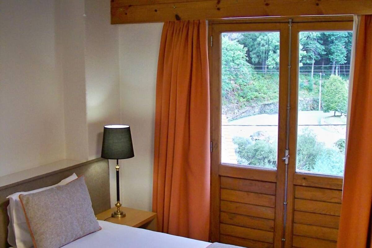 A double bed with a nightstand, a lamp, and a window with curtains.