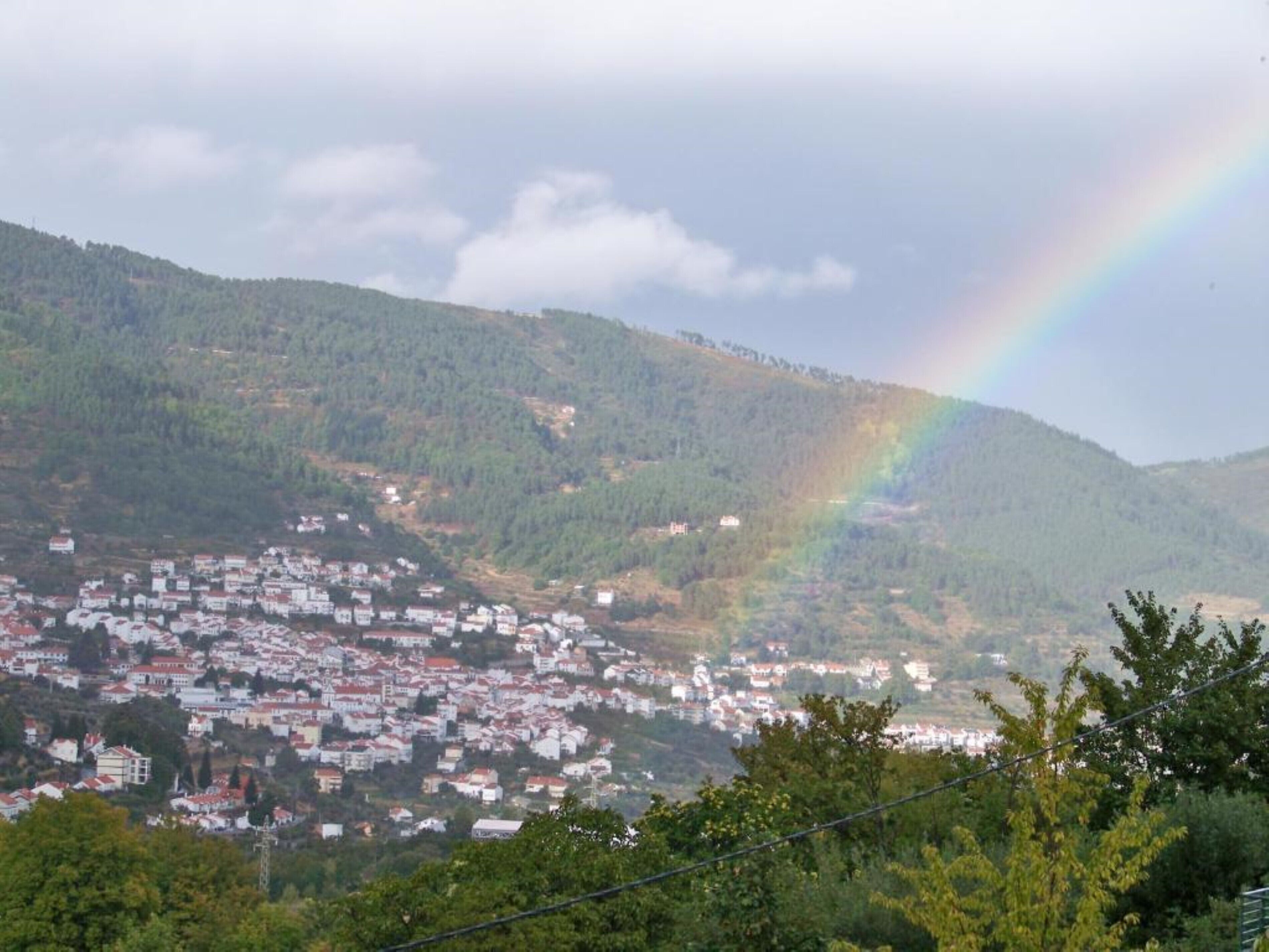 A town nestled in a valley with a mountain backdrop and a rainbow.