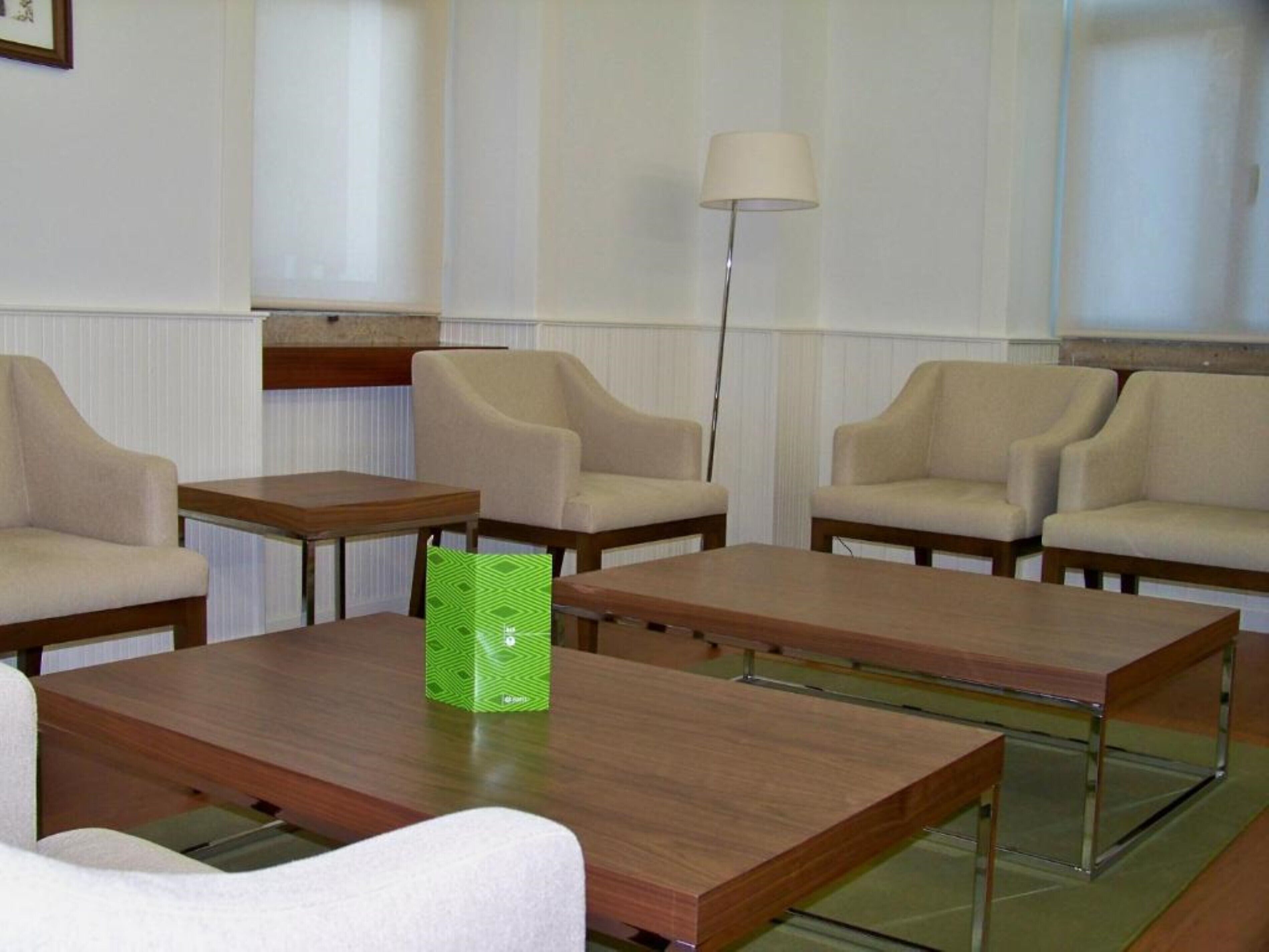 Una habitación de hotel con cuatro sillones color beige, dos mesas de madera y una lámpara de pie.