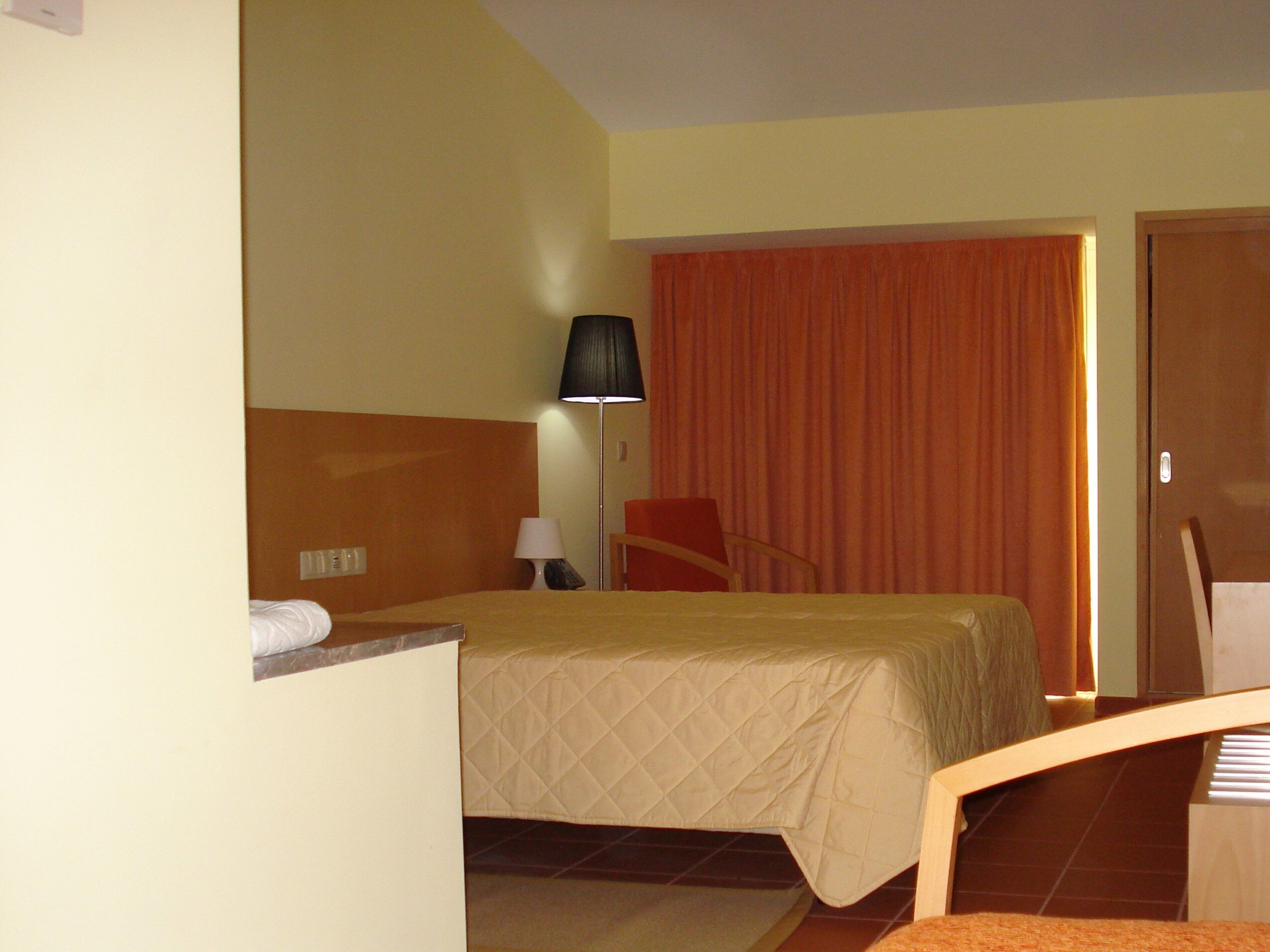 Una habitación de hotel con una cama, una silla, un escritorio, una lámpara y una puerta.