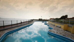 A swimming pool with a view of the sea, a fence, and a paved walkway. - INATEL Oeiras (Oeiras)