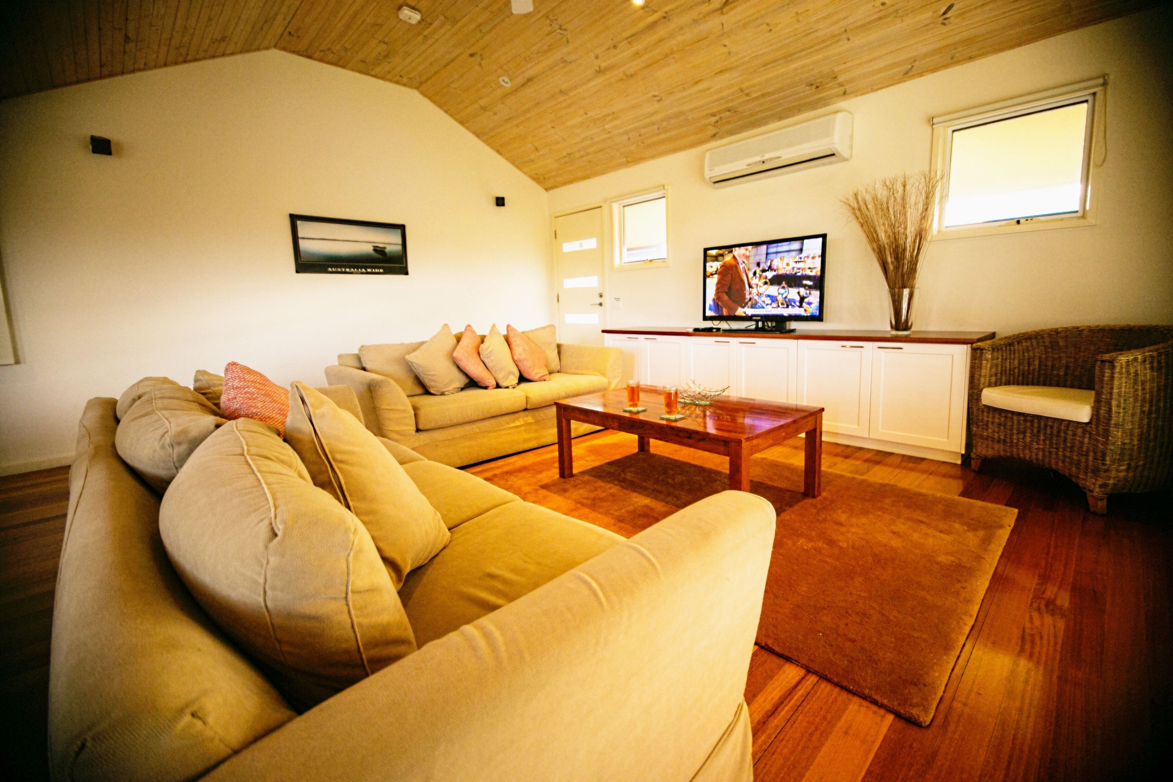 Een woonkamer met een beige bank, een houten salontafel en een rieten stoel.
