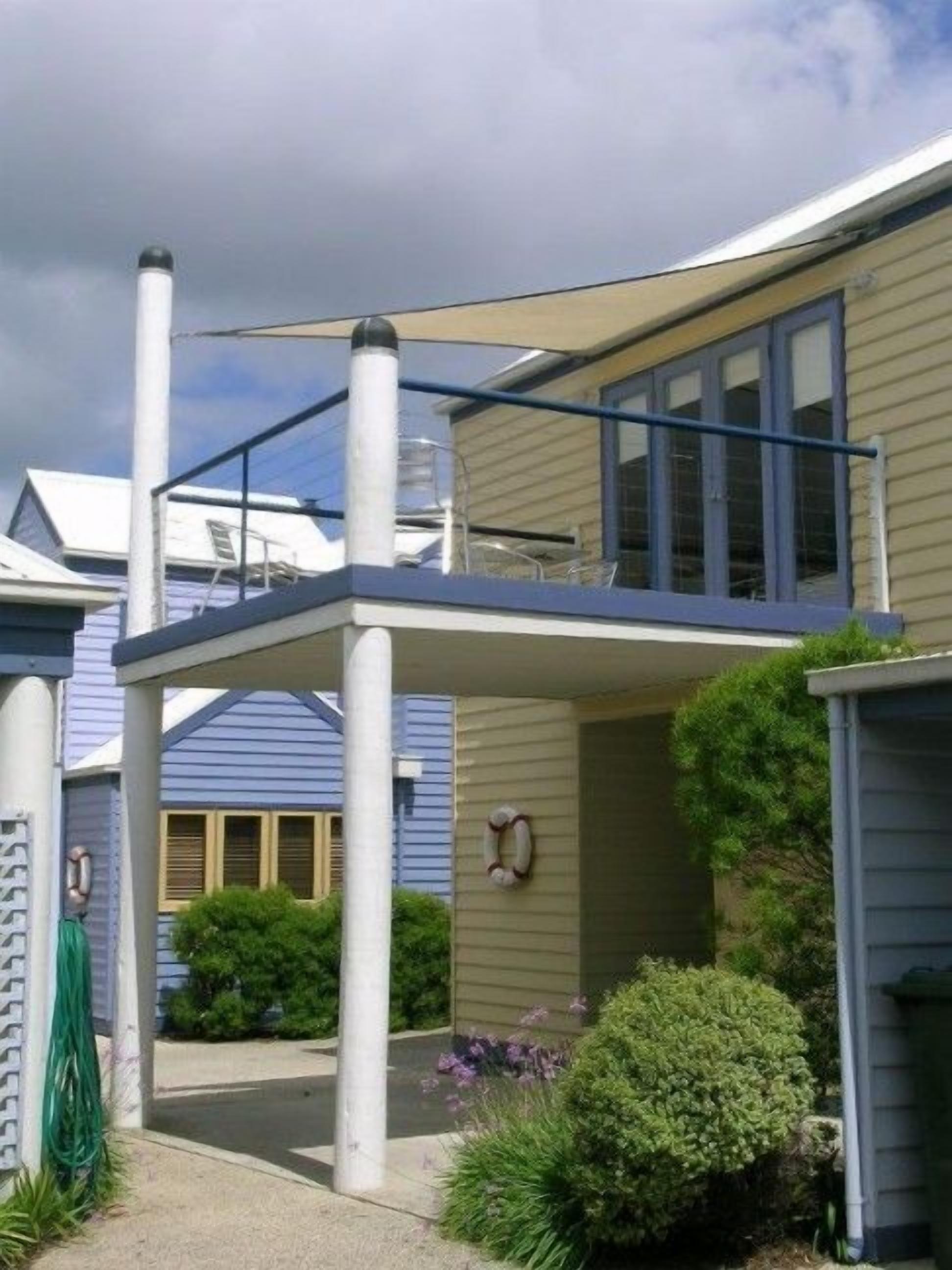 Un edificio residencial con un patio cubierto, un pequeño jardín y una ventana visible.
