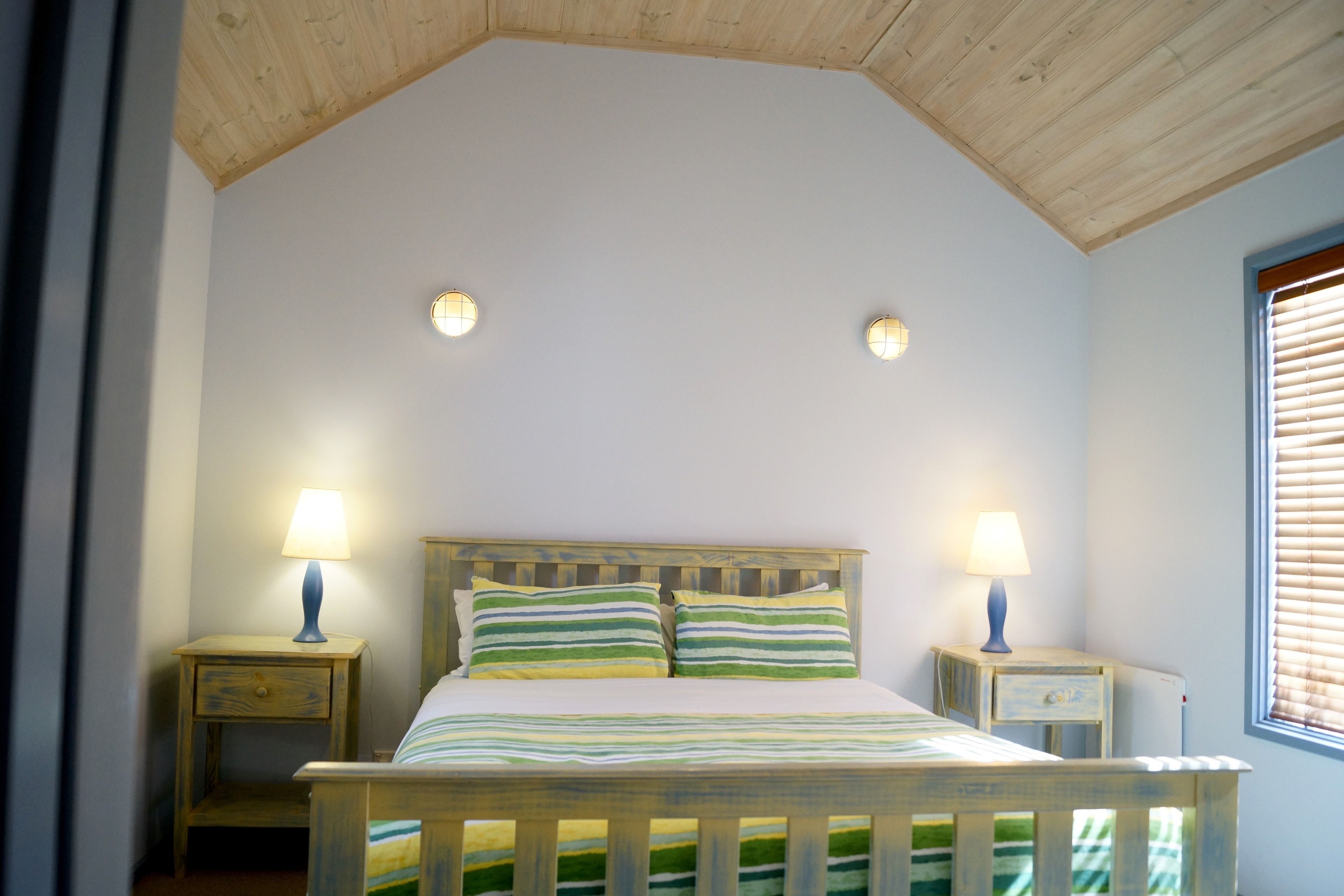 A bedroom with a wooden bed, two bedside tables with lamps, and a window with blinds.