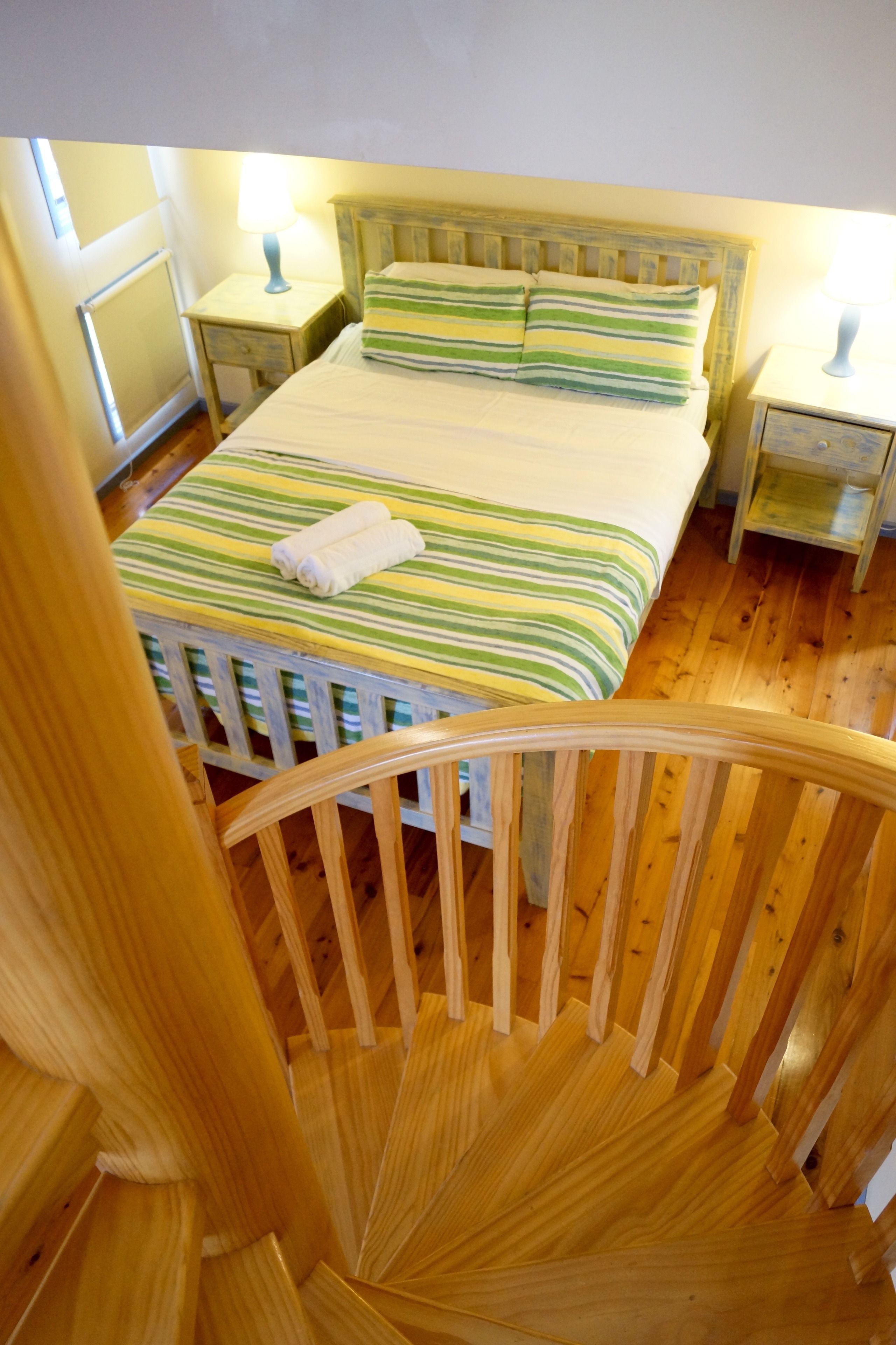 Un dormitorio con una cama de madera, ropa de cama a rayas, una mesita de noche y una lámpara.