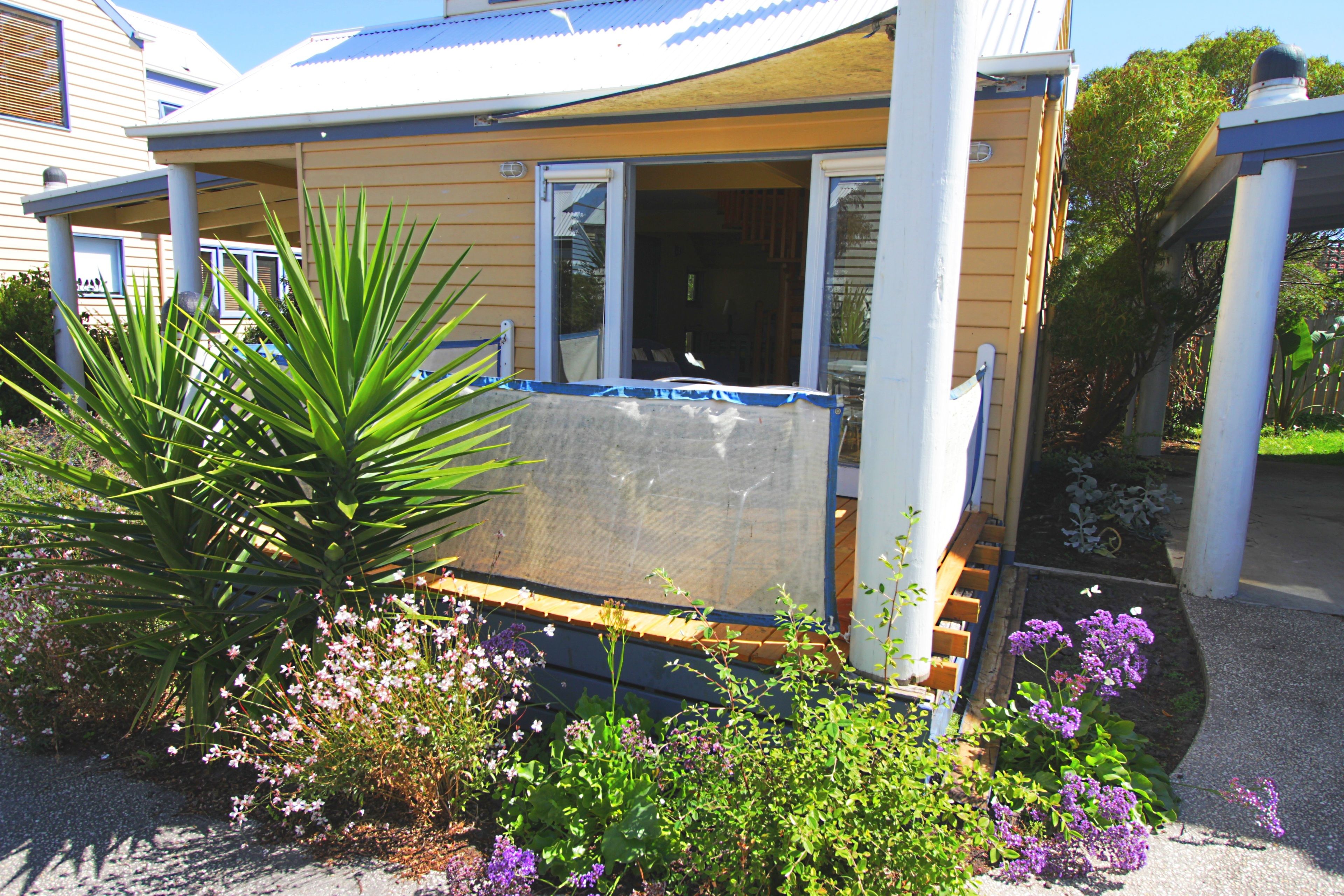 A house with a covered porch, a garden with various plants and flowers, and a clear sky.