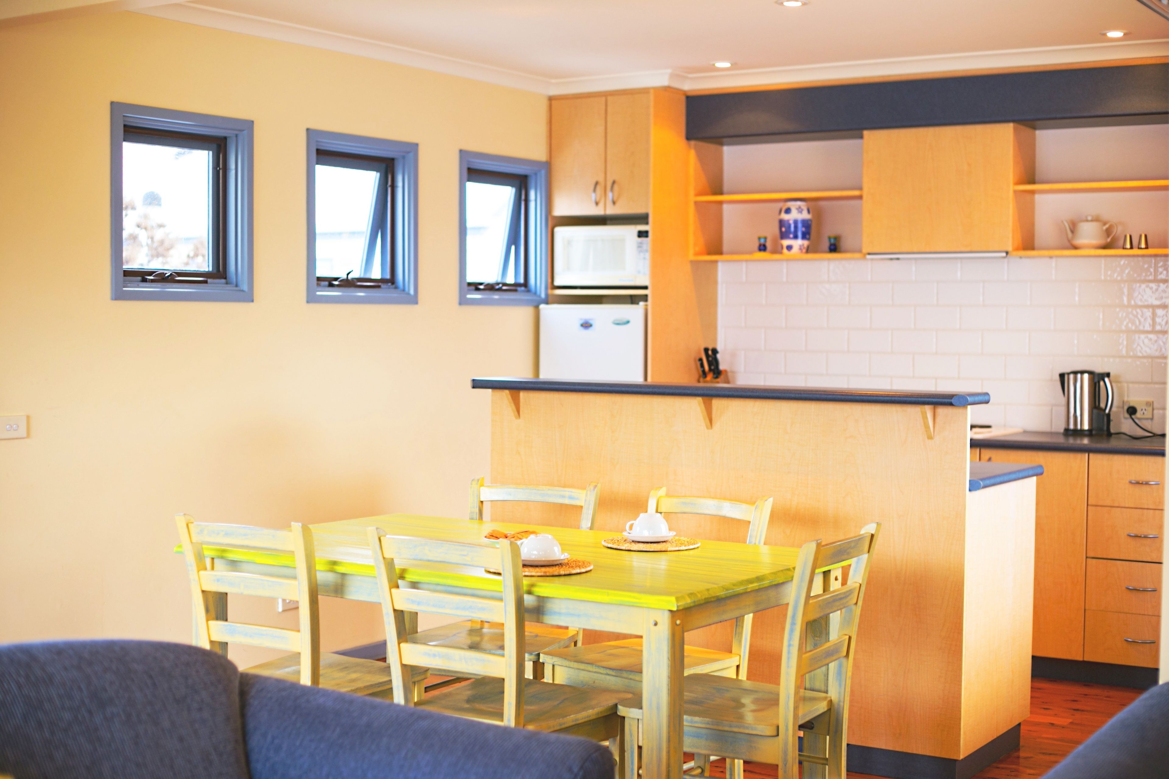 A compact kitchen with a dining area, featuring a small island, wooden cabinets, and a microwave.