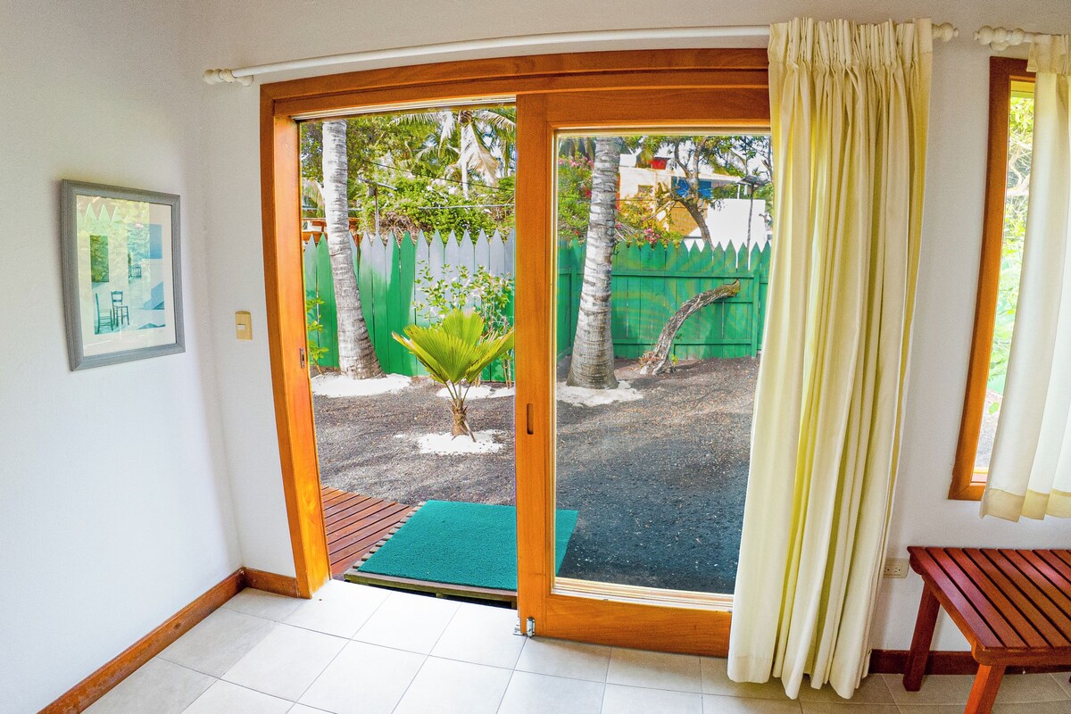 A room with a sliding glass door leading to a covered outdoor area with a bench and a small palm tree.