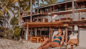 Un resort frente a la playa con un edificio de dos pisos, mobiliario exterior y palmeras.