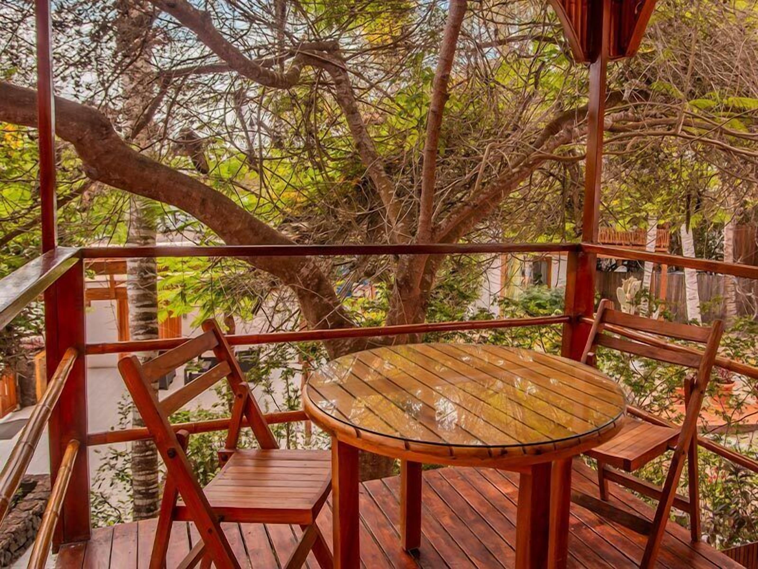 A wooden deck with a round table and chairs, surrounded by trees.