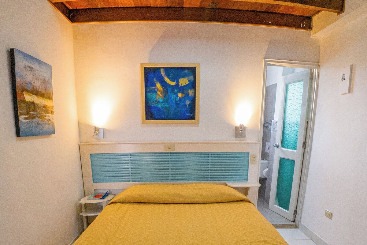 A bedroom with a bed, a painting, a nightstand, and a door.