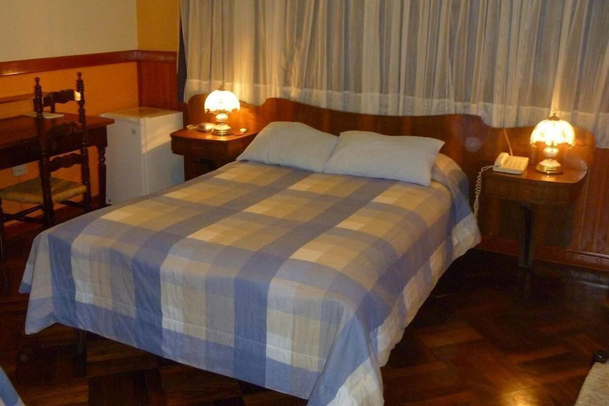 A hotel room with a bed, two bedside tables with lamps, a chair, and a desk with a telephone.