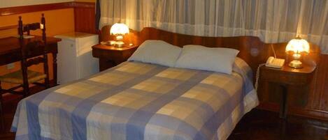 A hotel room with a bed, two bedside tables with lamps, a chair, and a desk with a telephone.
