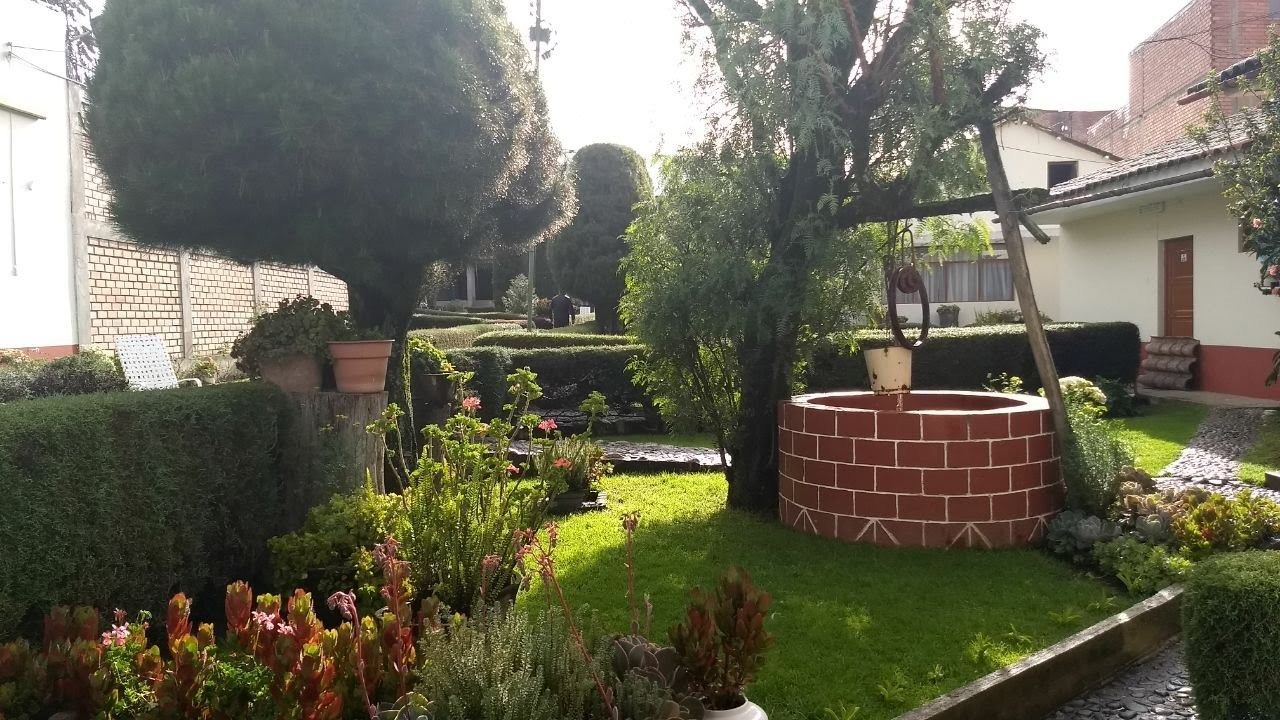 Un jardín bien cuidado con una estructura circular de ladrillo, setos podados y diversas plantas.