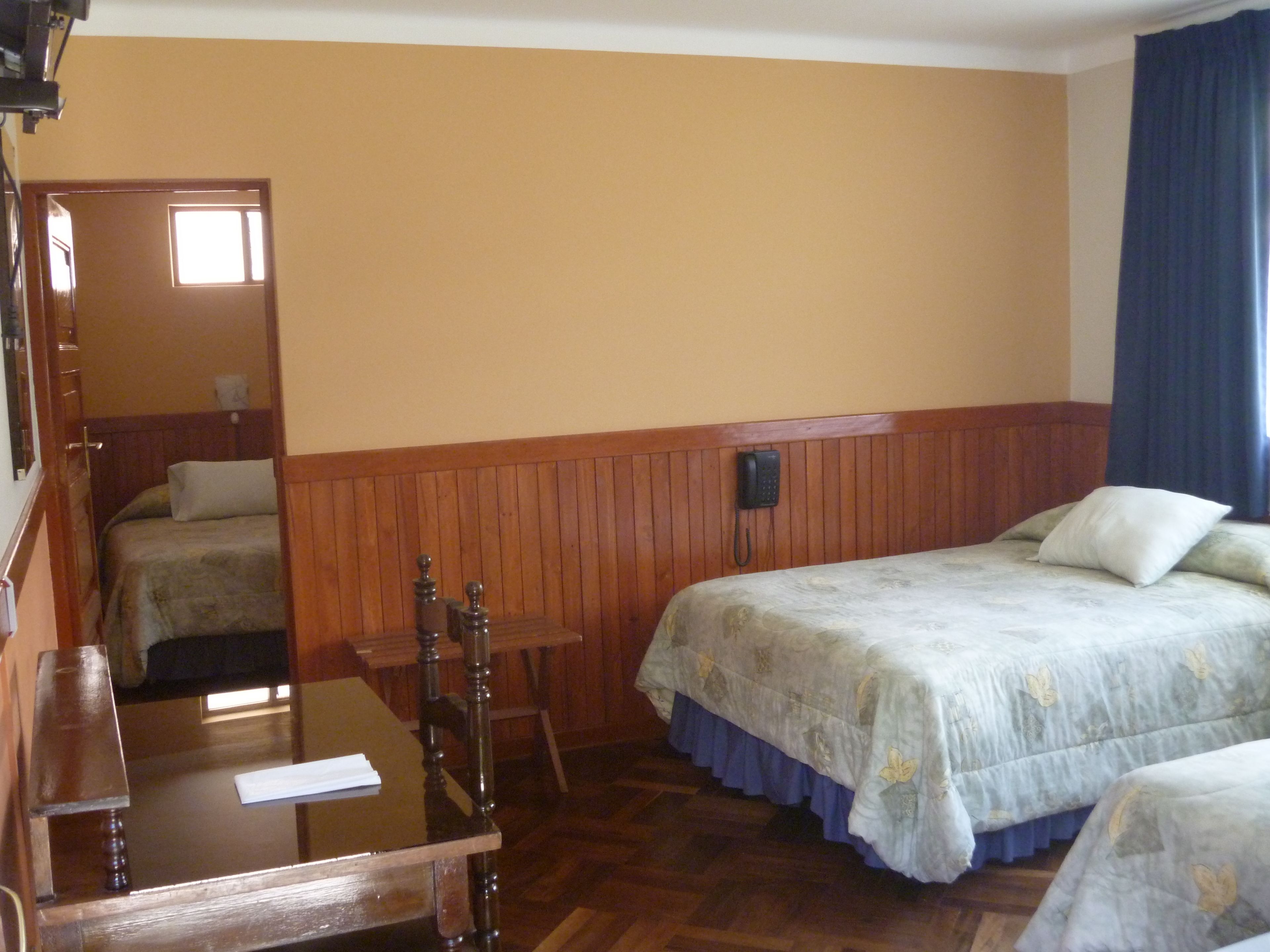 A hotel room with two beds, a wooden table, a chair, and a telephone.