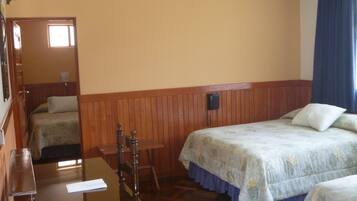 A hotel room with two beds, a wooden table, a chair, and a telephone.