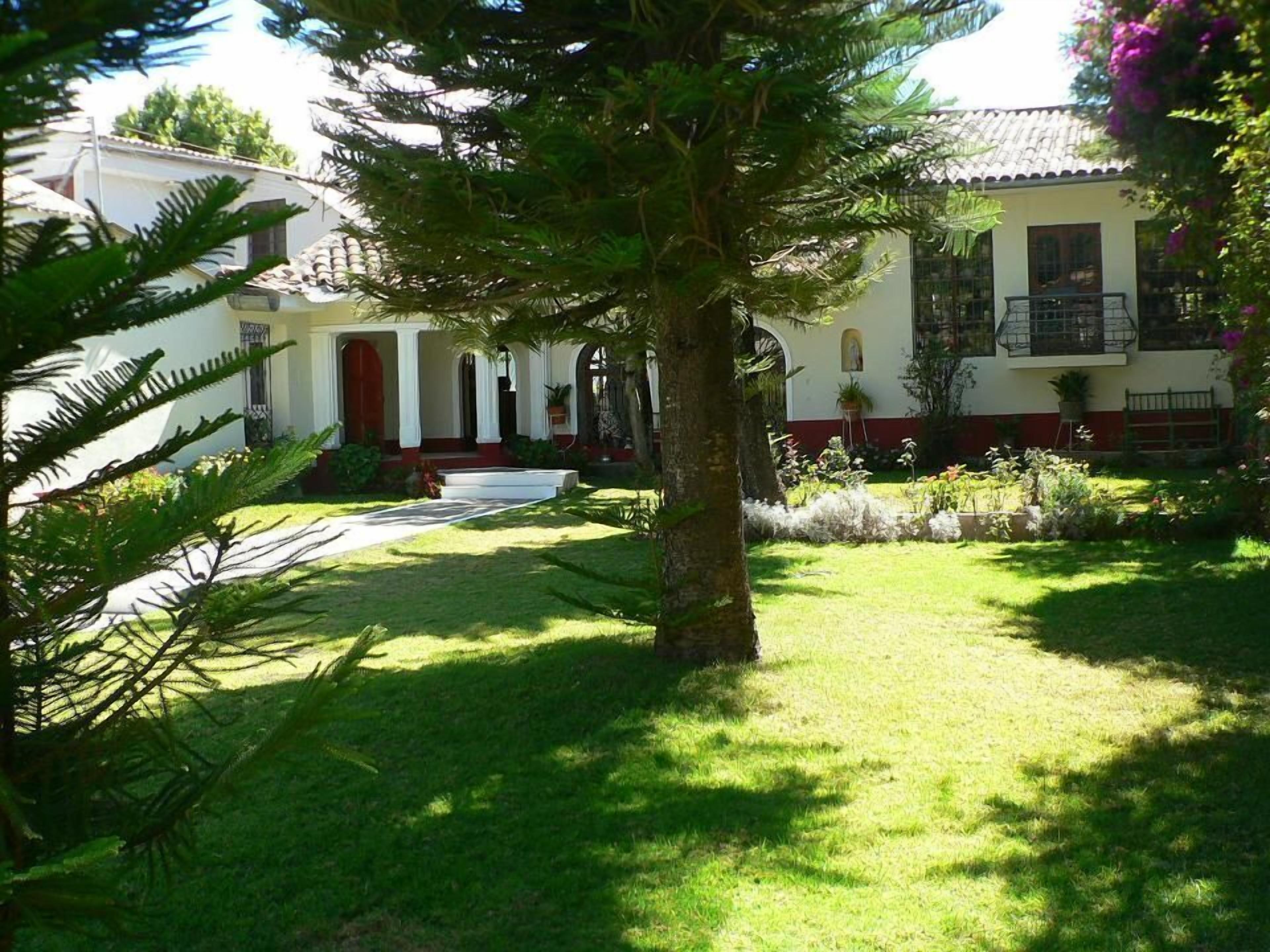 A well-maintained garden with a large tree, a pathway, and a building with a red door and white walls.