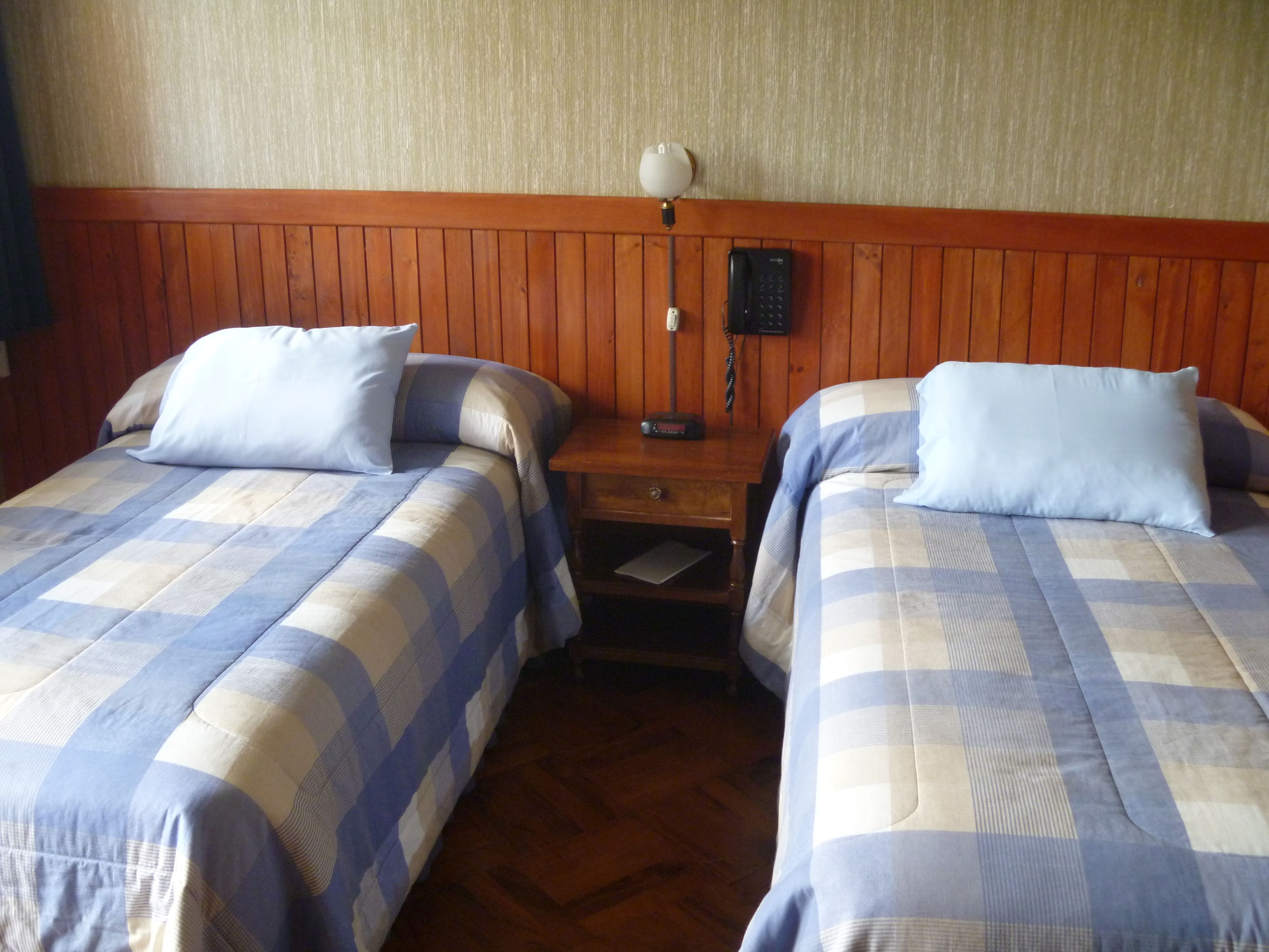 A hotel room with two beds, each with a checkered bedspread, a nightstand with a lamp, and a telephone.
