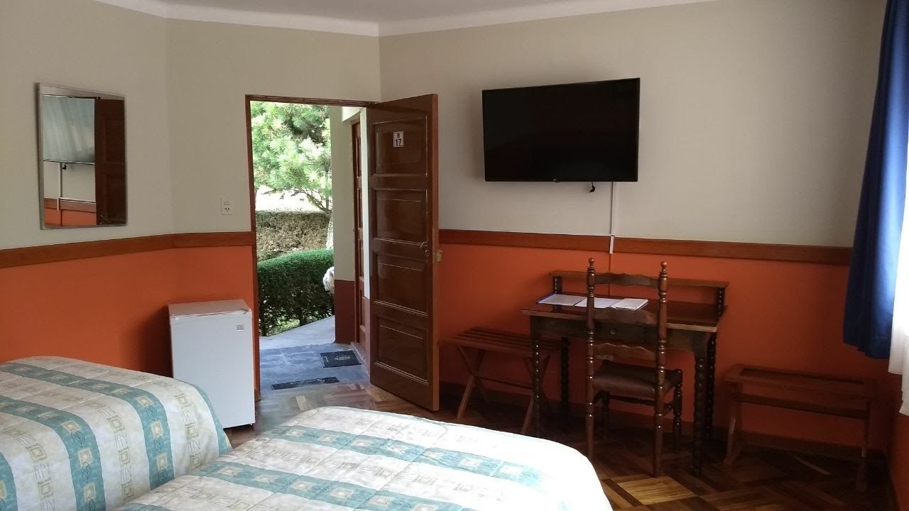 A hotel room with a bed, a desk, a television, and a small refrigerator.