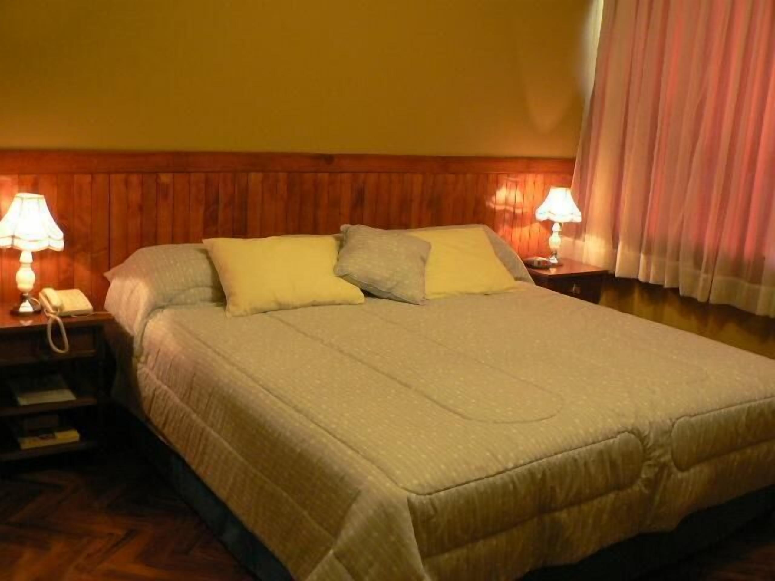 A neatly made bed with a beige comforter and pillows, a wooden headboard, and bedside lamps.