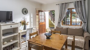 A living room with a wooden dining table, chairs, a sofa, a television, and a clock on the wall. - Algoa Guesthouse Summerstrand (Port Elizabeth)