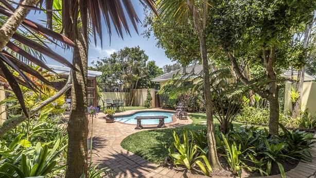A garden with a swimming pool, a stone bench, and various plants. - Algoa Guesthouse Summerstrand (Port Elizabeth)