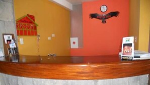 A reception desk with a wooden counter, a clock on the wall, and a red wall with a bird mural. - Kuntur Inn (Puno)