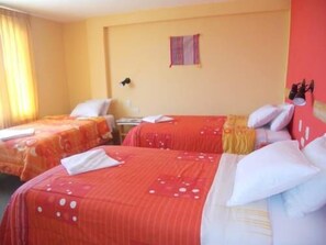 A hotel room with two beds, each with red bedding and white pillows. There is a small table and a wall-mounted lamp.