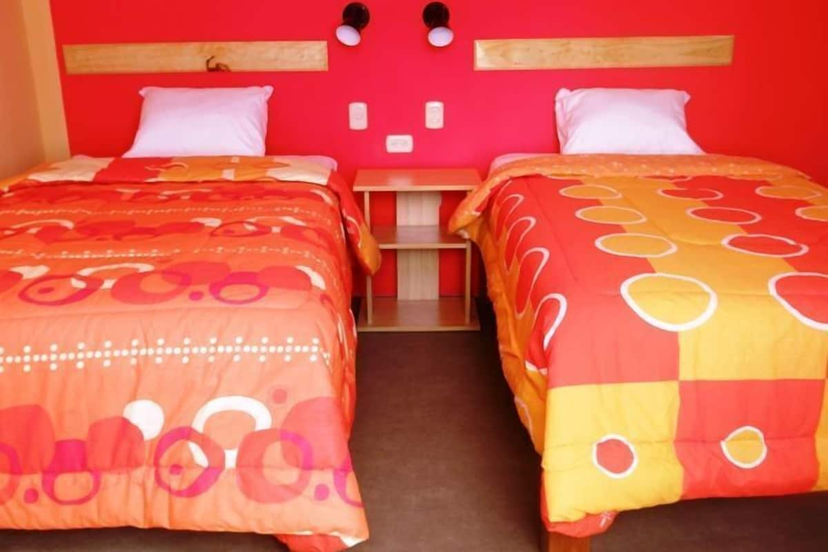 A room with two beds, each with a red and orange patterned bedspread, wooden headboards, and white pillows.
