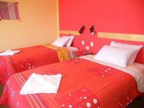 A hotel room with two beds, each with red bedding and white pillows. There is a small table with a phone and a lamp.