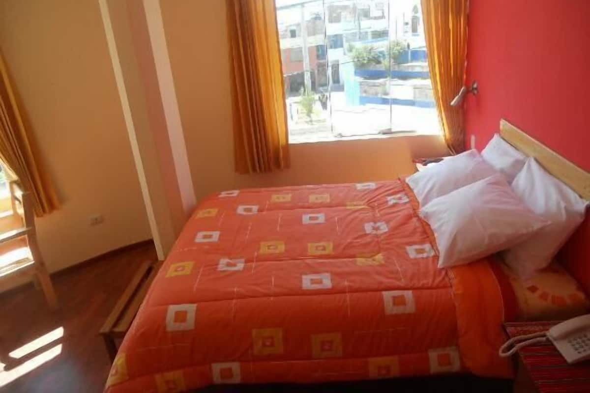 A bedroom with a bed, a window with curtains, and a telephone on the bedside table.