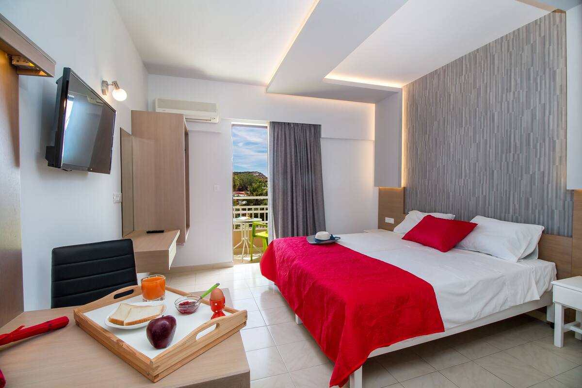Una habitación de hotel moderna con cama, televisor, bandeja de desayuno y balcón con vistas.