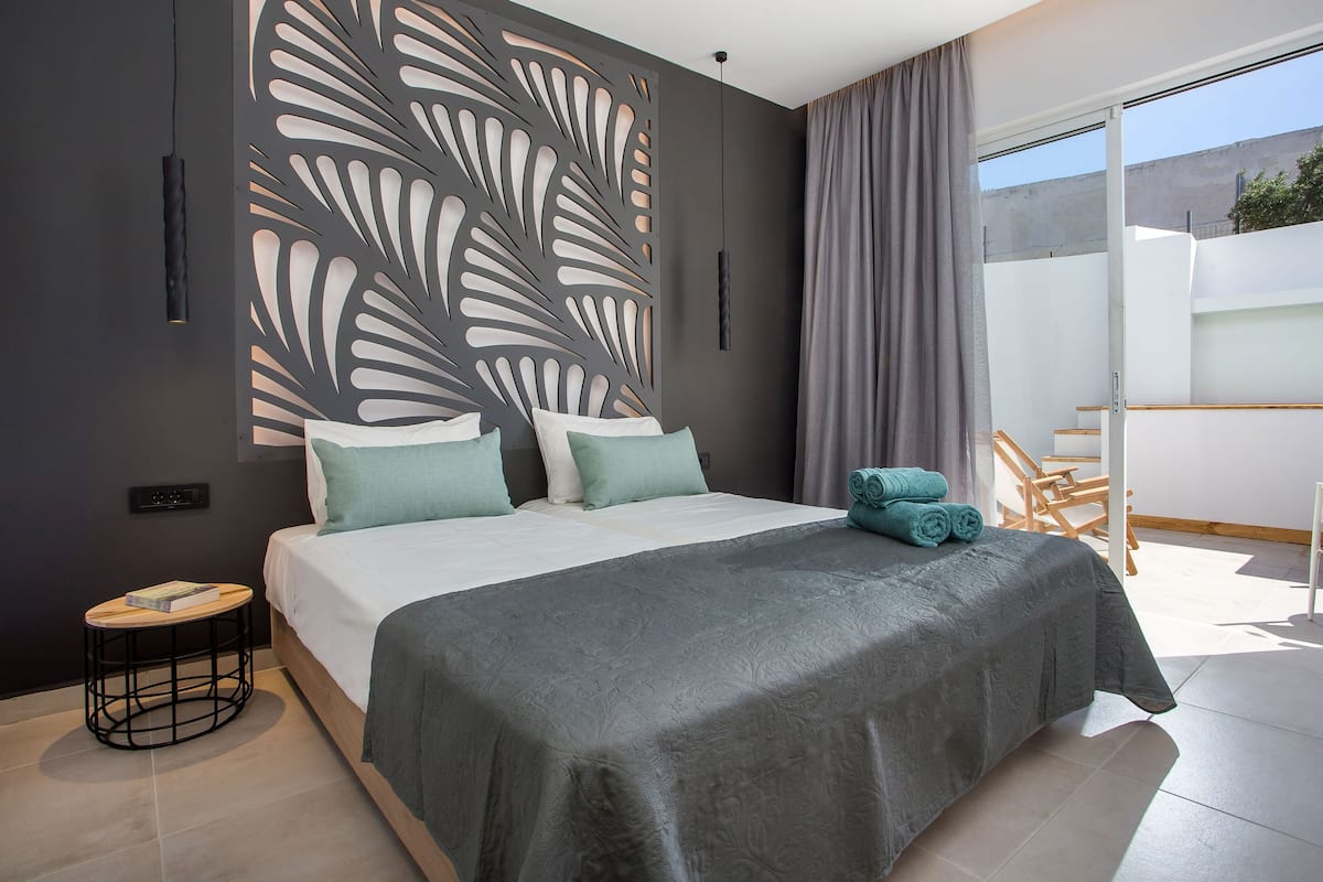Un dormitorio moderno con una cama grande, un panel decorativo en la pared, una pequeña mesa redonda y vistas al exterior mediante una puerta corredera.