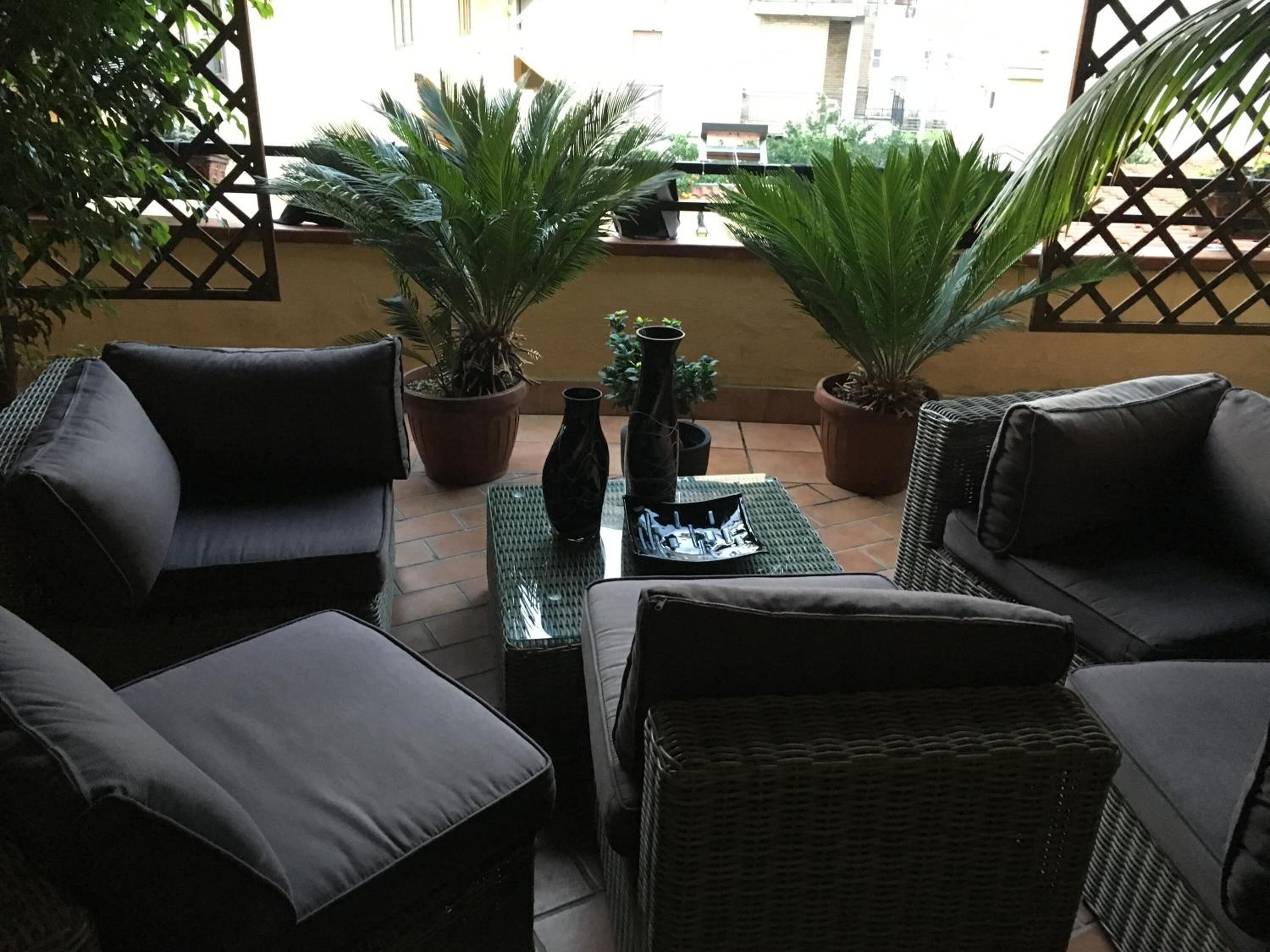 A patio with wicker furniture, potted plants, and a tiled floor.