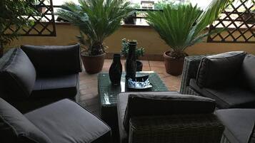 A patio with wicker furniture, potted plants, and a tiled floor.