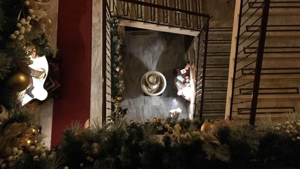 A decorated Christmas tree with ornaments and lights, a stone wall with a circular design, and a staircase with a metal railing. - Hotel Amadeus (Caserta)