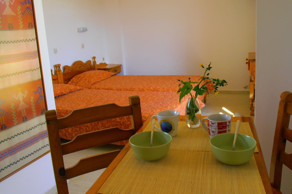 A room with a bed, a table with green bowls, a mug, and a vase with a plant.